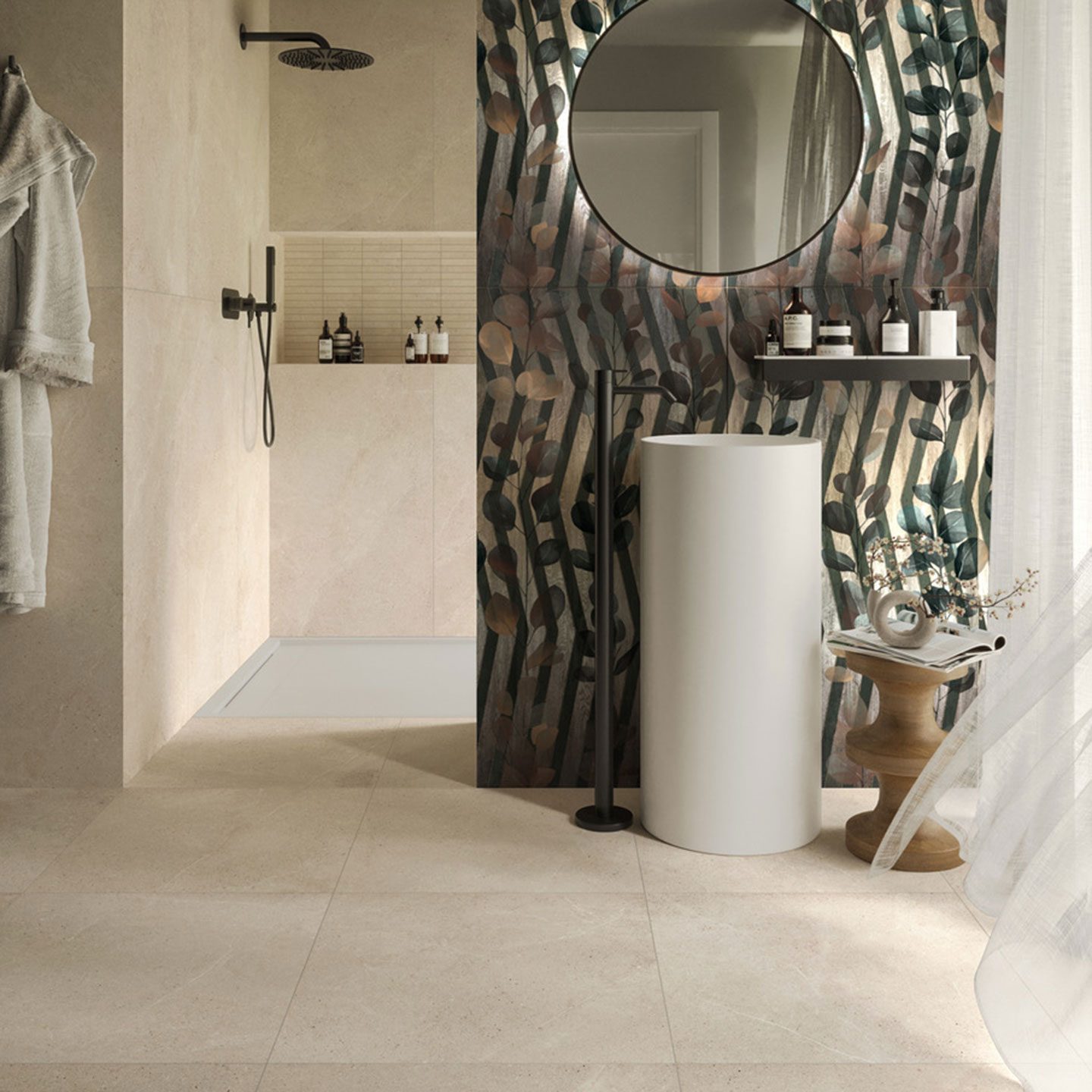 Interno di un bagno moderno con lavabo a colonna bianco e rubinetteria nera opaca. La parete di fondo presenta un decoro artistico con motivi botanici e linee grafiche verticali, abbinata a rivestimenti e pavimento in ceramica color sabbia.