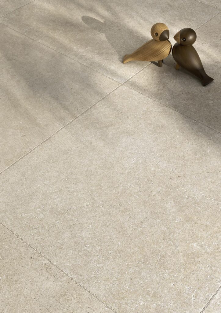 Particolare del pavimento della collezione Cathédrale, variante Reims Blanc nel formato 60x60. Due uccellini decorativi in legno poggiano sulla superficie bianca opaca effetto pietra, creando un'atmosfera poetica.