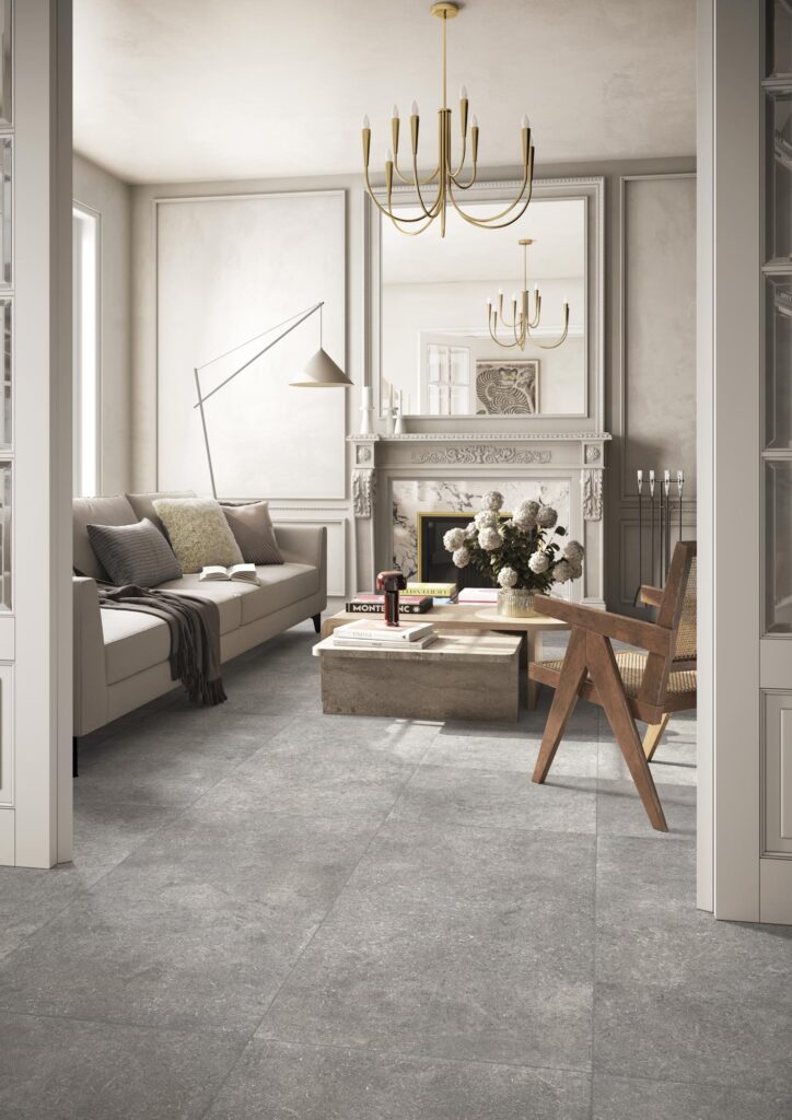 Elegante zona living con pavimento della collezione Cathédrale, variante Amiens Acier nel formato 60x120. Le grandi lastre grigie creano continuità visiva in un soggiorno con camino classico e arredi ricercati.