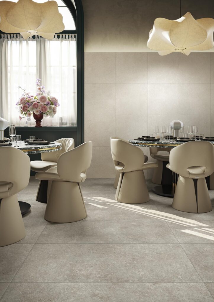 Ambiente ristorante di lusso che combina la collezione Cathédrale nei colori Rouen Corde (formato 60x120) e Reims Blanc (formato 60x60). La pavimentazione grigia e beige definisce uno spazio elegante con tavoli rotondi e sedute di design.