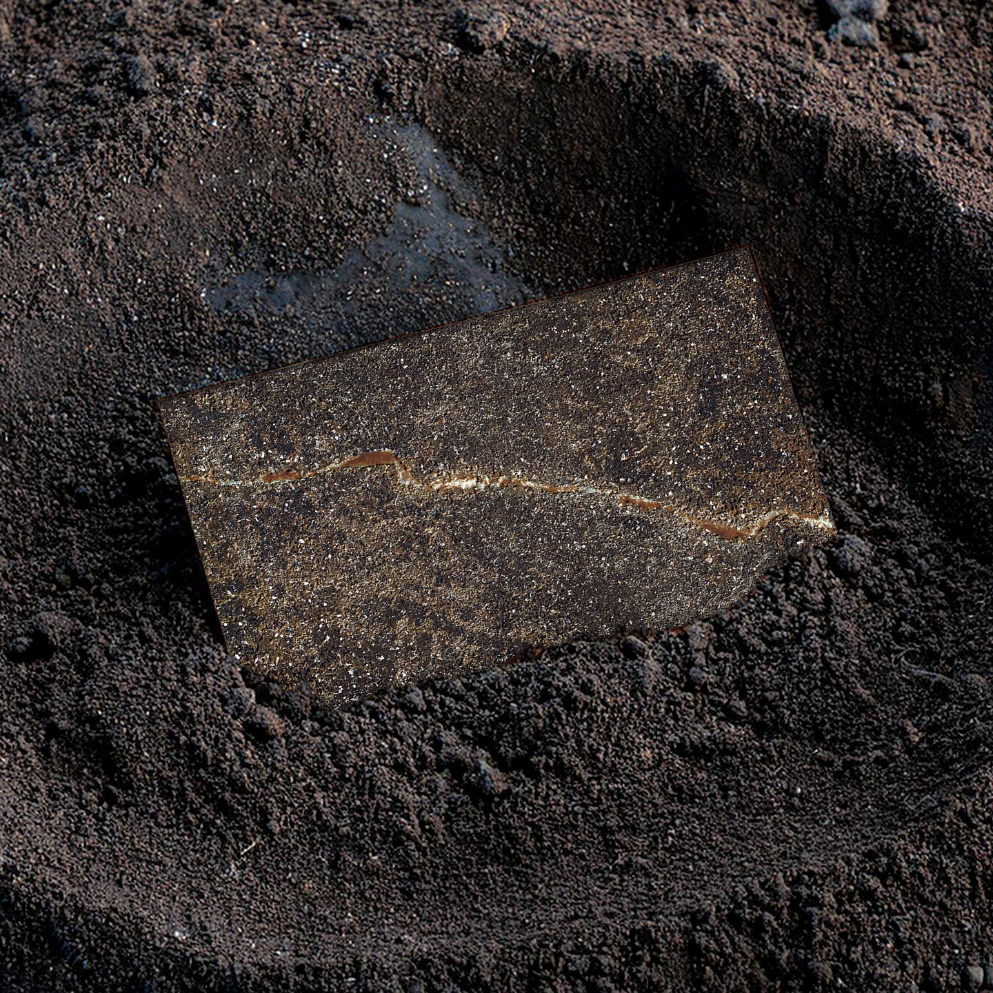 Immagine di una piastrella in gres porcellanato della serie G_Tech, appoggiata nella polvere d'argilla da cui sembra nascere